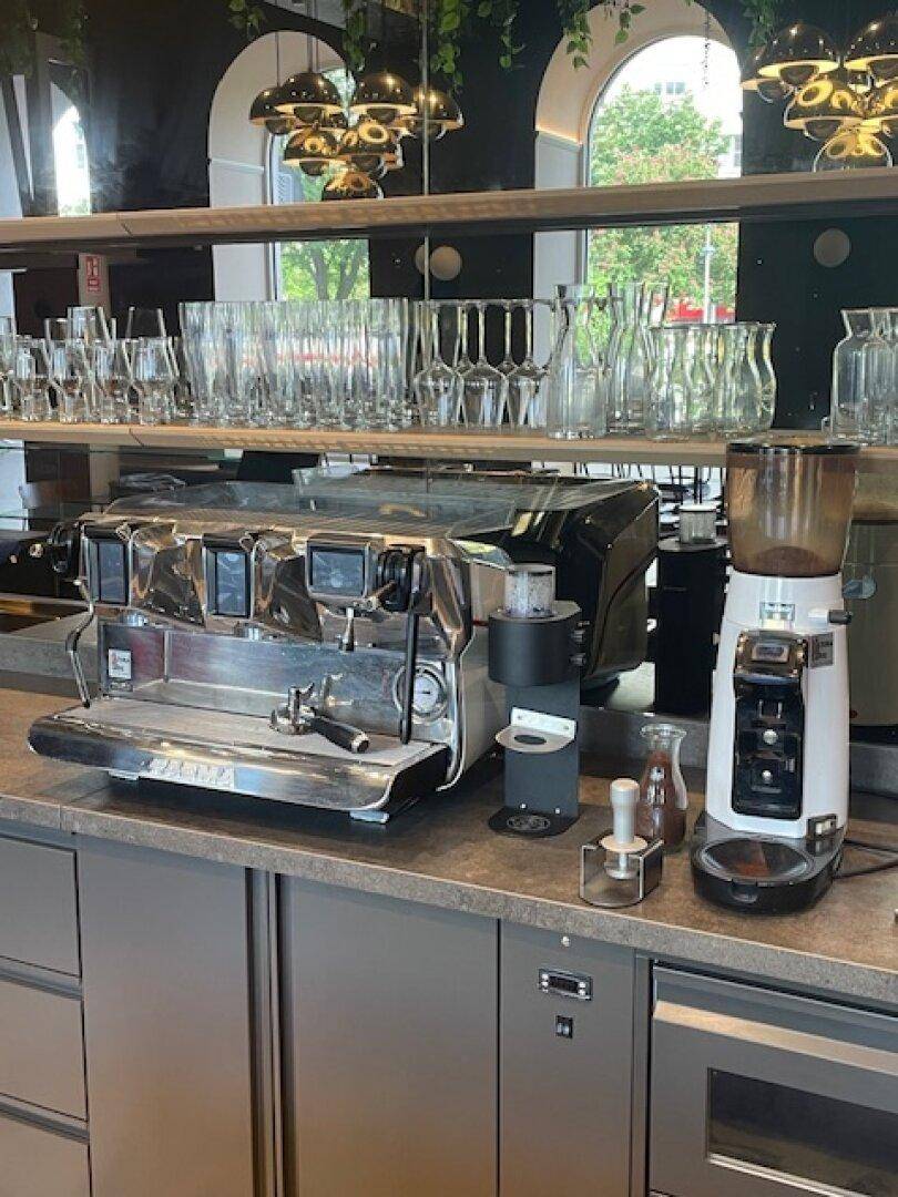 Kaffeestation in einer Gewerbeküche mit professioneller Espressomaschine, Kaffeemühle und Gläsern.