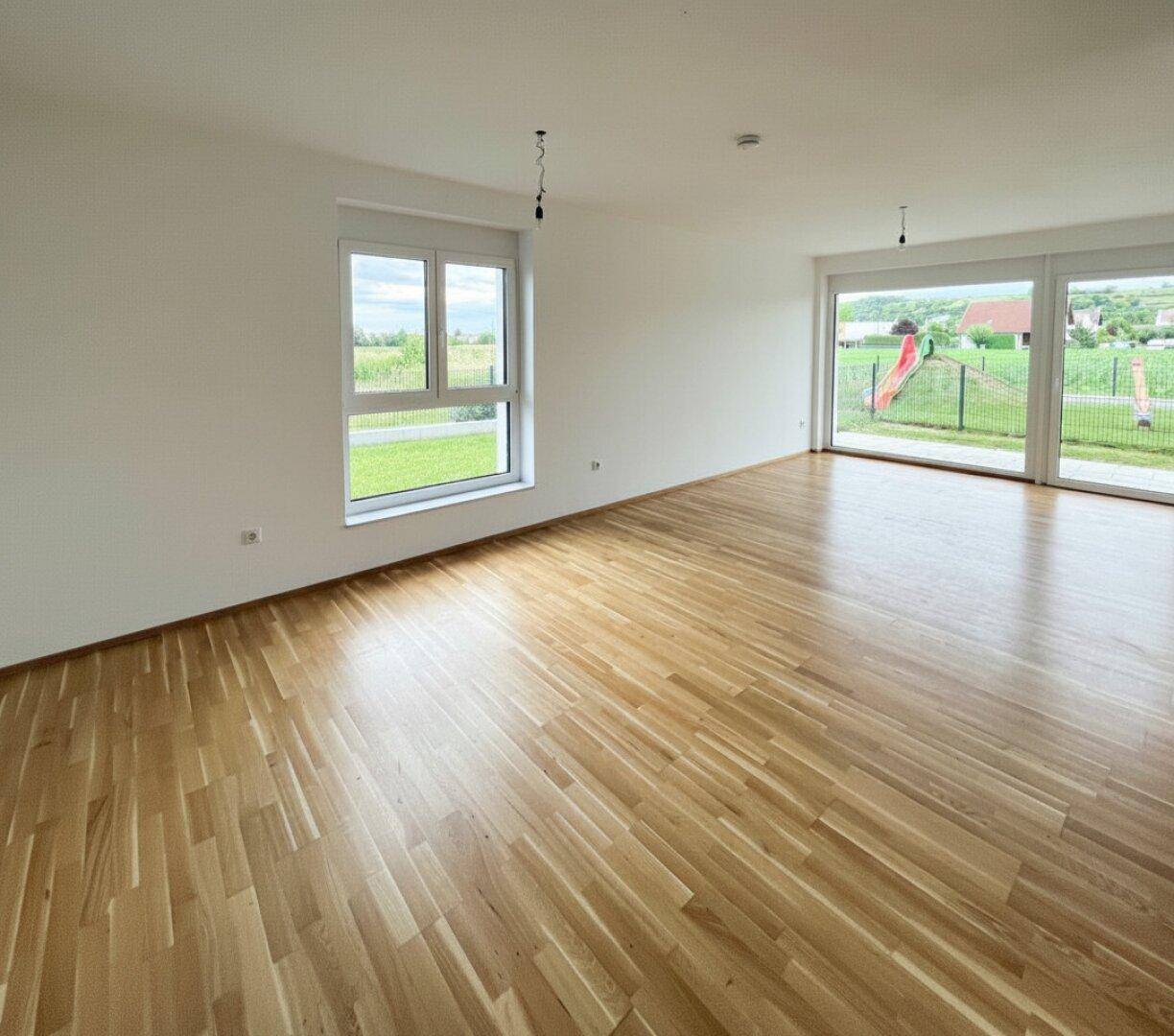 Heller, unmöblierter Wohnbereich mit großen Fenstern und Holzboden, bereit zur individuellen Gestaltung.
