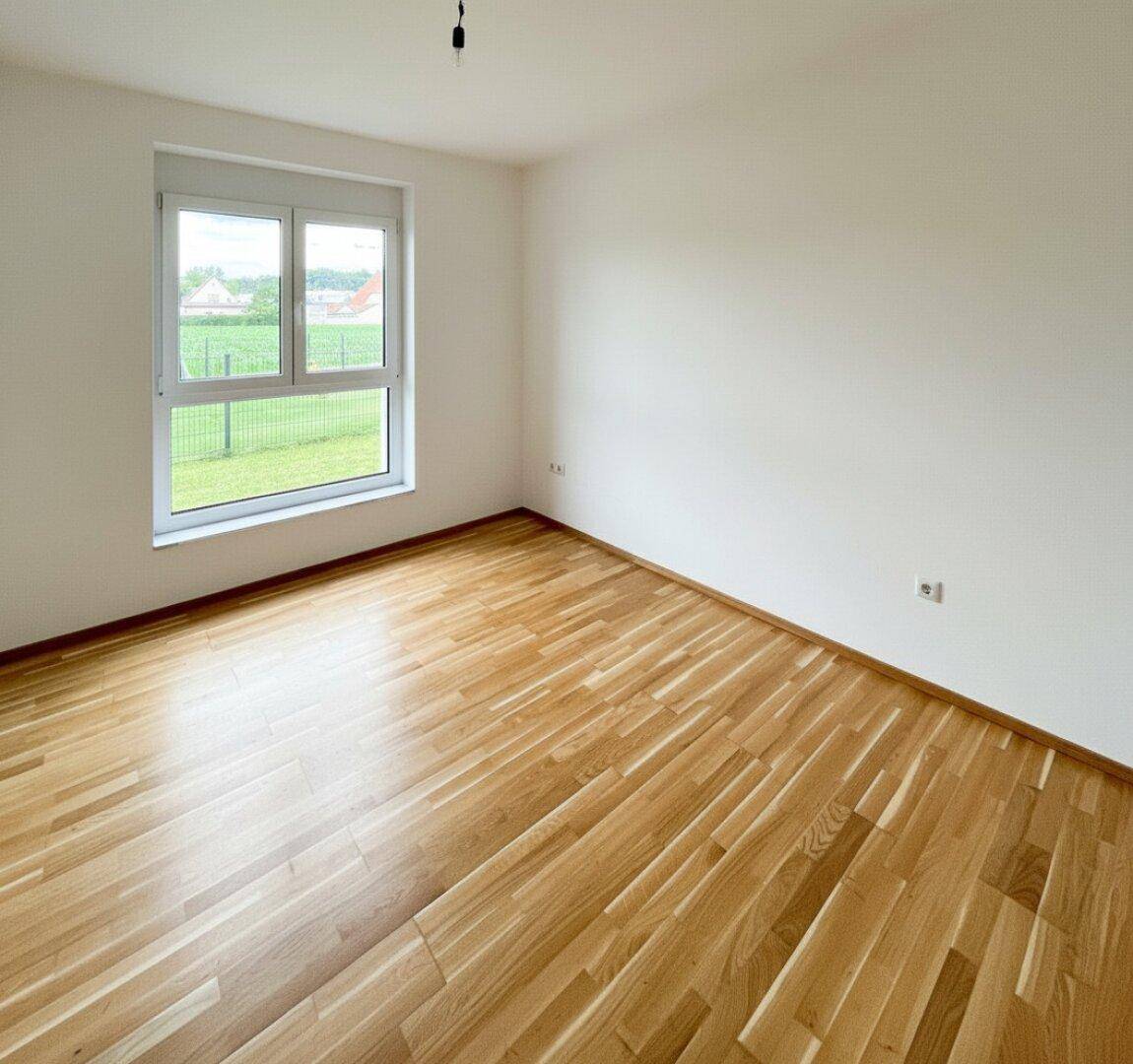 Unmöbliertes Zimmer mit Holzboden und großem Fenster, ideal als Schlaf- oder Arbeitszimmer.