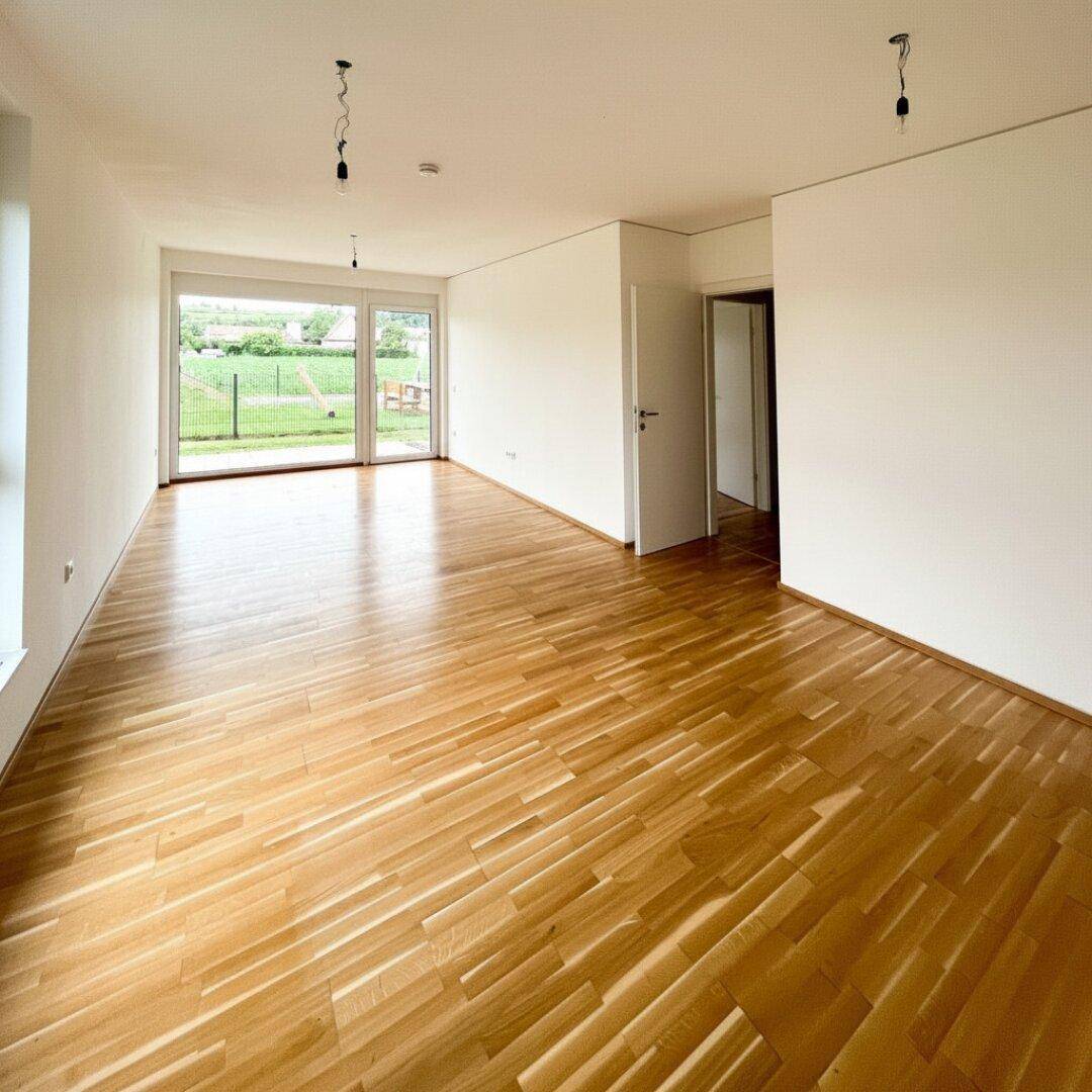 Geräumiger, unmöblierter Wohnbereich mit Holzboden und Zugang zu einem Außenbereich.