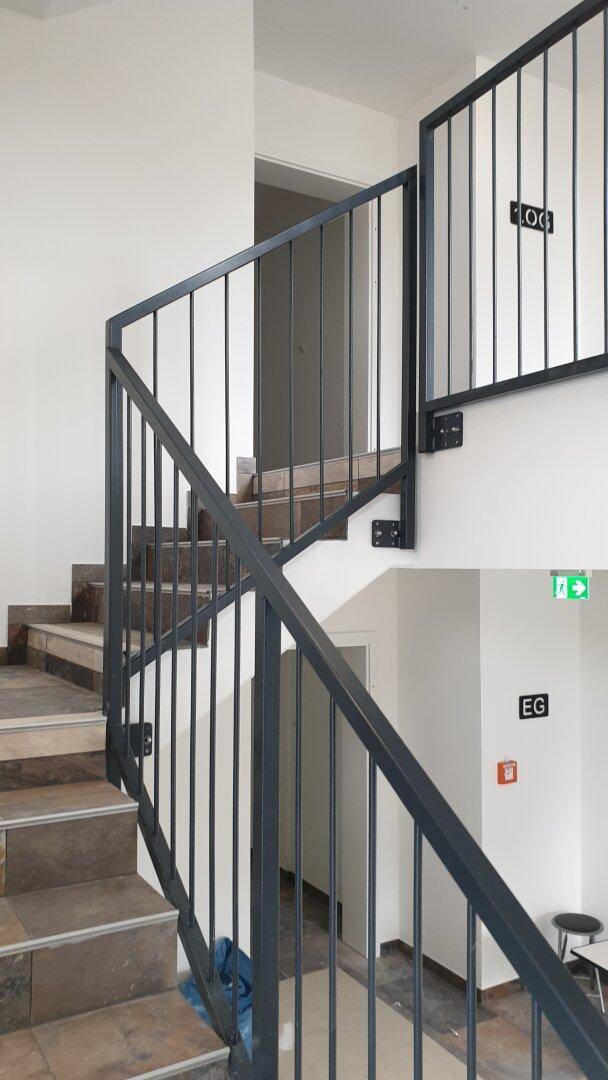 Modernes Treppenhaus mit dunklem Metallgeländer und Fliesenstufen in einem hellen Gebäude.