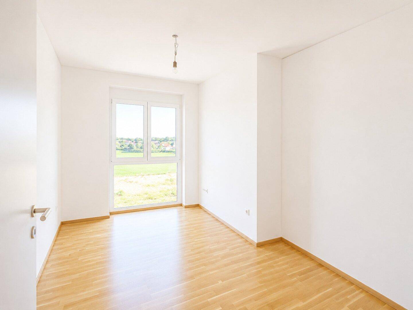 Leeres Schlafzimmer mit Holzboden und großem Fenster, das eine helle und offene Atmosphäre schafft.