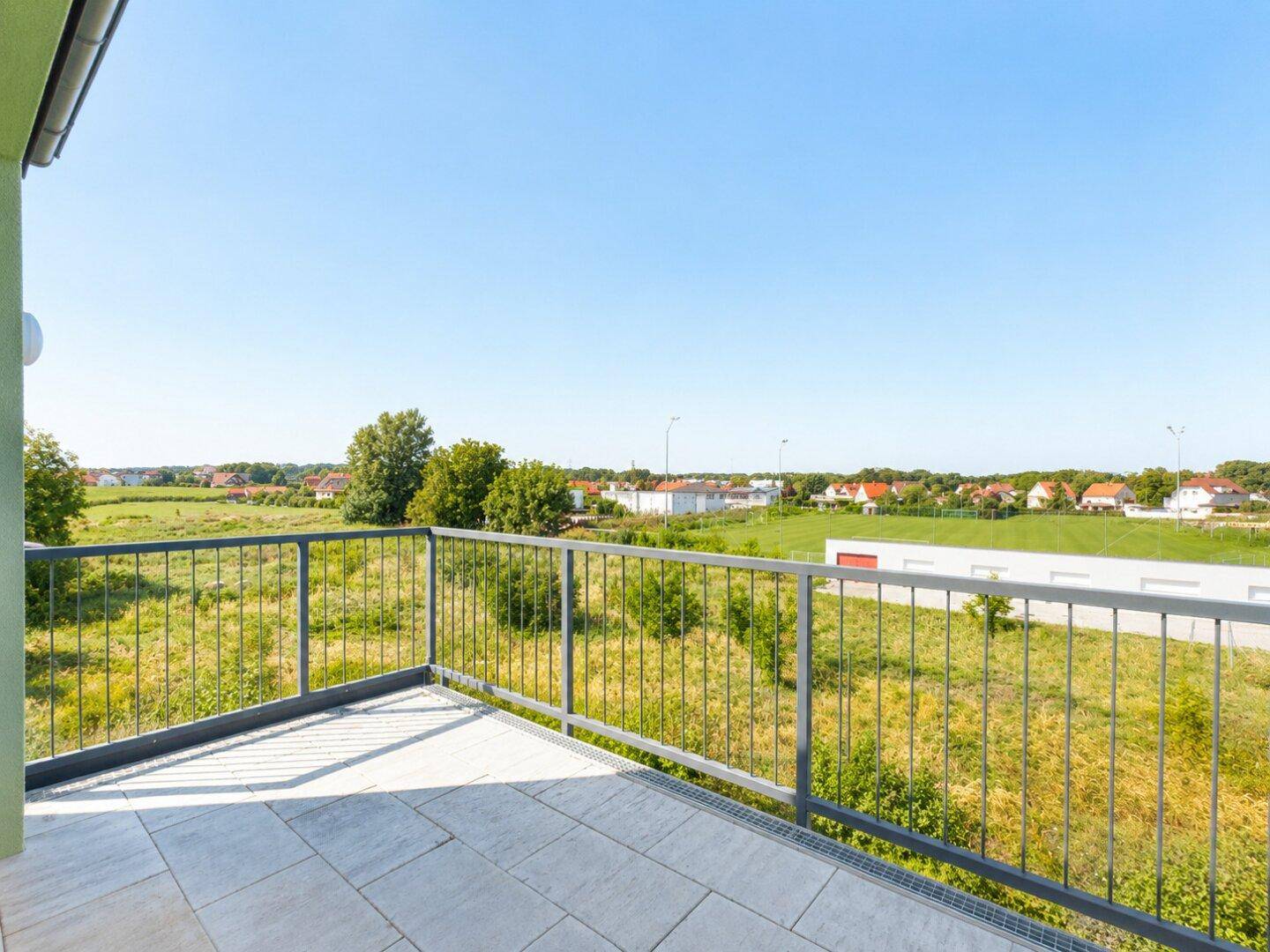 Geräumiger Balkon mit Fliesenboden und Metallgeländer, bietet weite Aussicht ins Grüne.