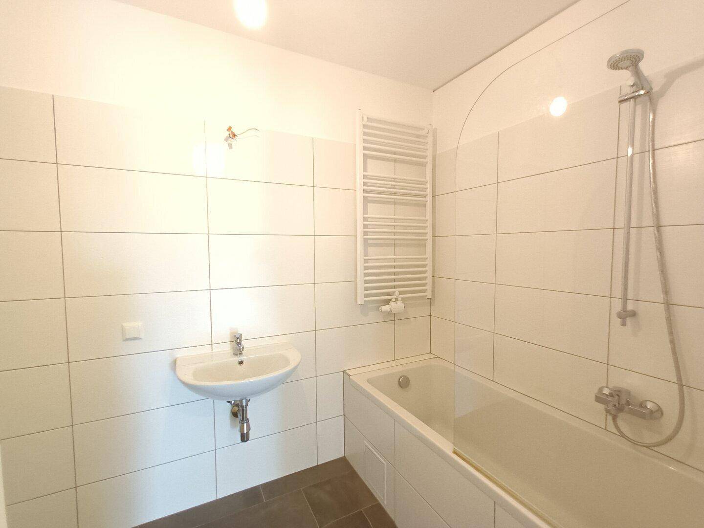 Helles Badezimmer mit weißen Fliesen, Badewanne und Handtuchheizkörper, unmöbliert.
