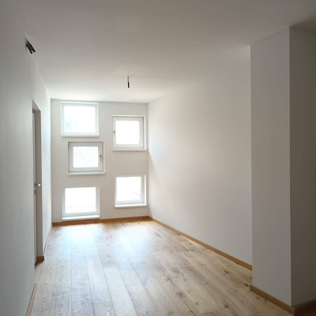 Leerer Raum mit hellem Holzboden und mehreren Fenstern, bereit für individuelle Gestaltung.