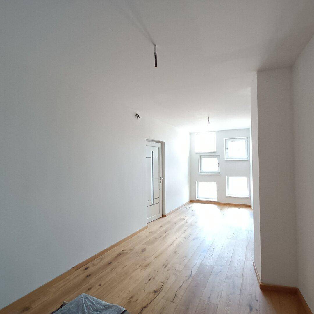 Heller Flur mit Holzboden und natürlichem Lichteinfall durch mehrere Fenster am Ende.