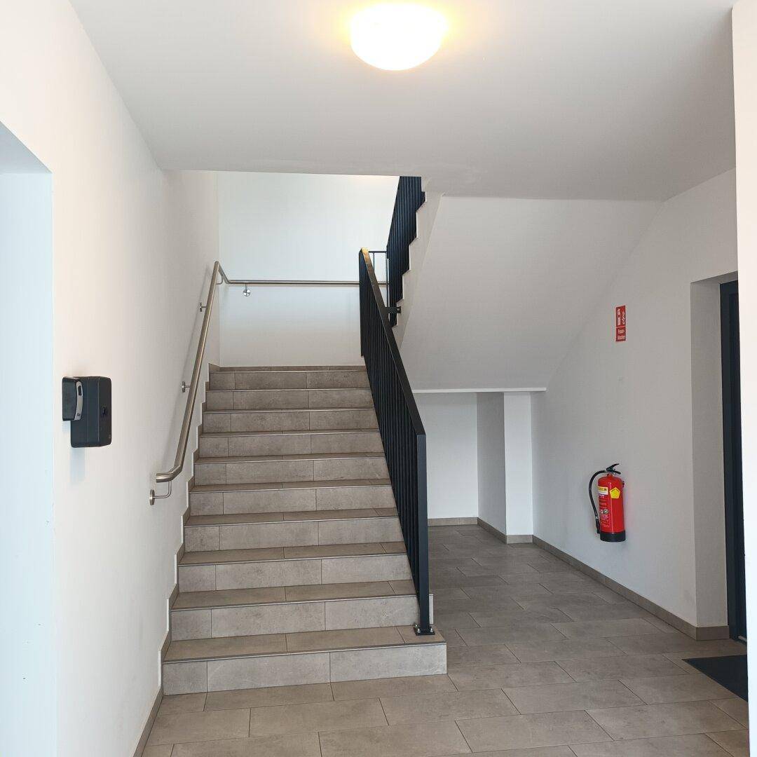 Treppenhaus mit gefliesten Stufen, modernen Metallgeländern und einem Feuerlöscher.