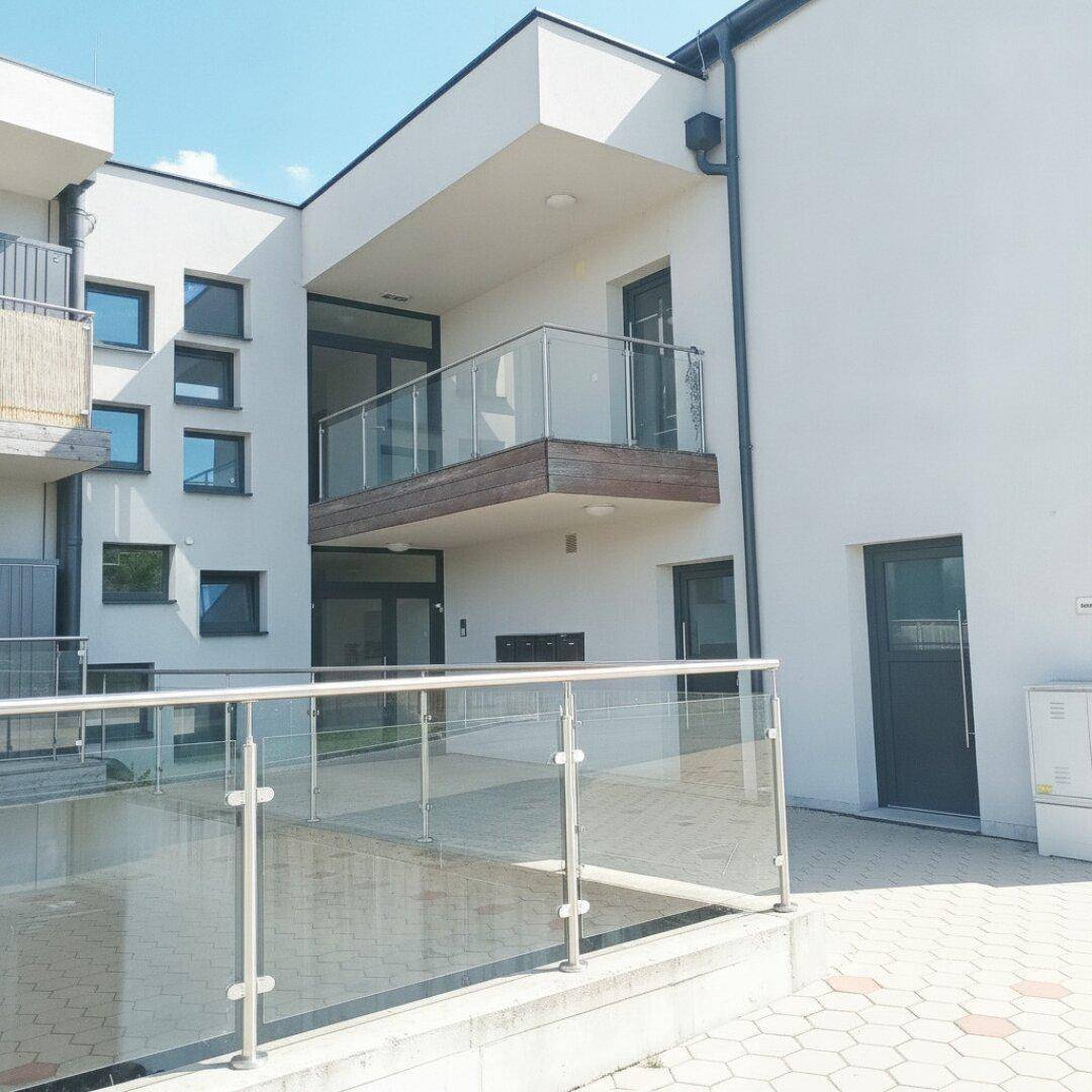 Modernes Gebäude mit Balkonen, Glasgeländern und gepflastertem Außenbereich.
