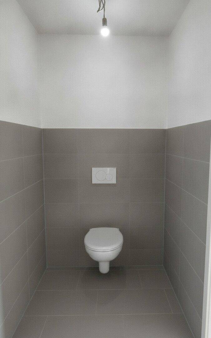 Modernes Gäste-WC mit wandhängender Toilette und grauen Fliesen an den Wänden.