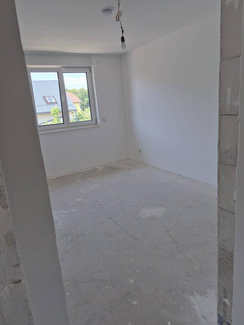 Unfertiges Schlafzimmer mit Fenster und Blick auf die Dächer der Nachbarhäuser.
