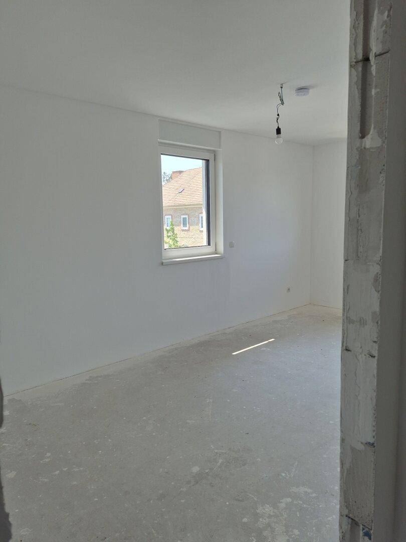 Unfertiges Schlafzimmer mit Fenster und Blick auf die umliegenden Häuser und Bäume.