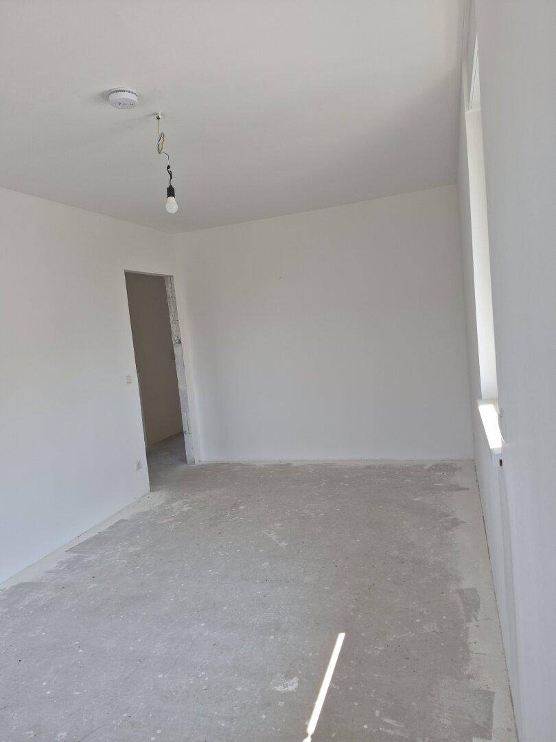 Unfertiges Schlafzimmer mit weiß gestrichenen Wänden und einem Fenster für natürliches Licht.