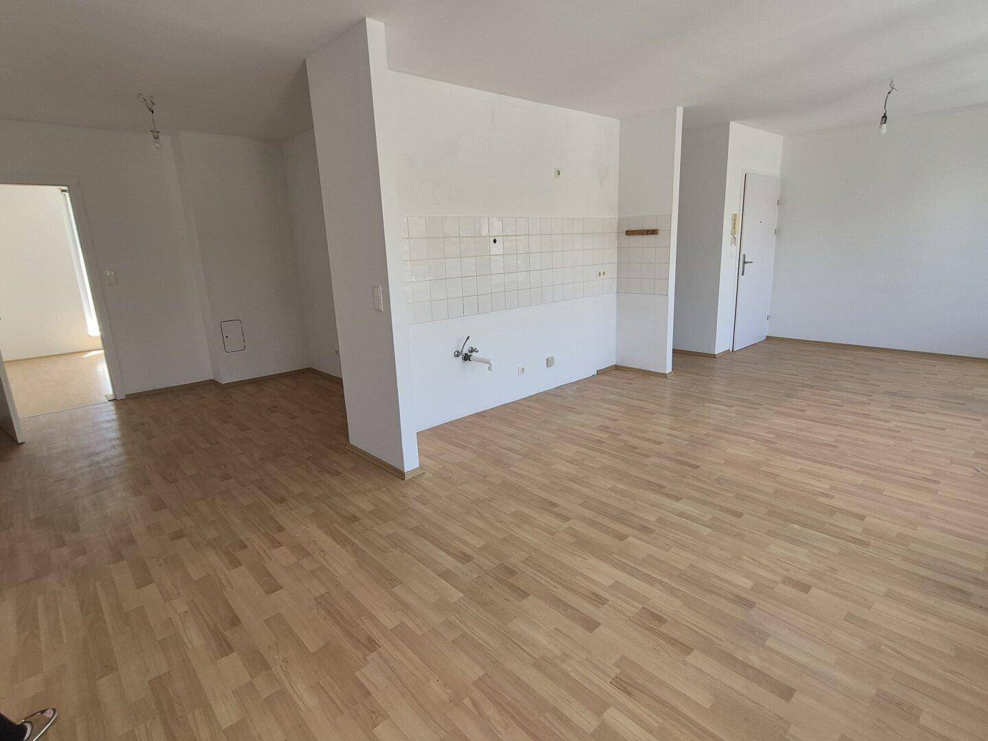 Offener Wohnbereich mit Holzparkett und vorbereiteter Küchenzeile, ideal für modernes Wohnen.