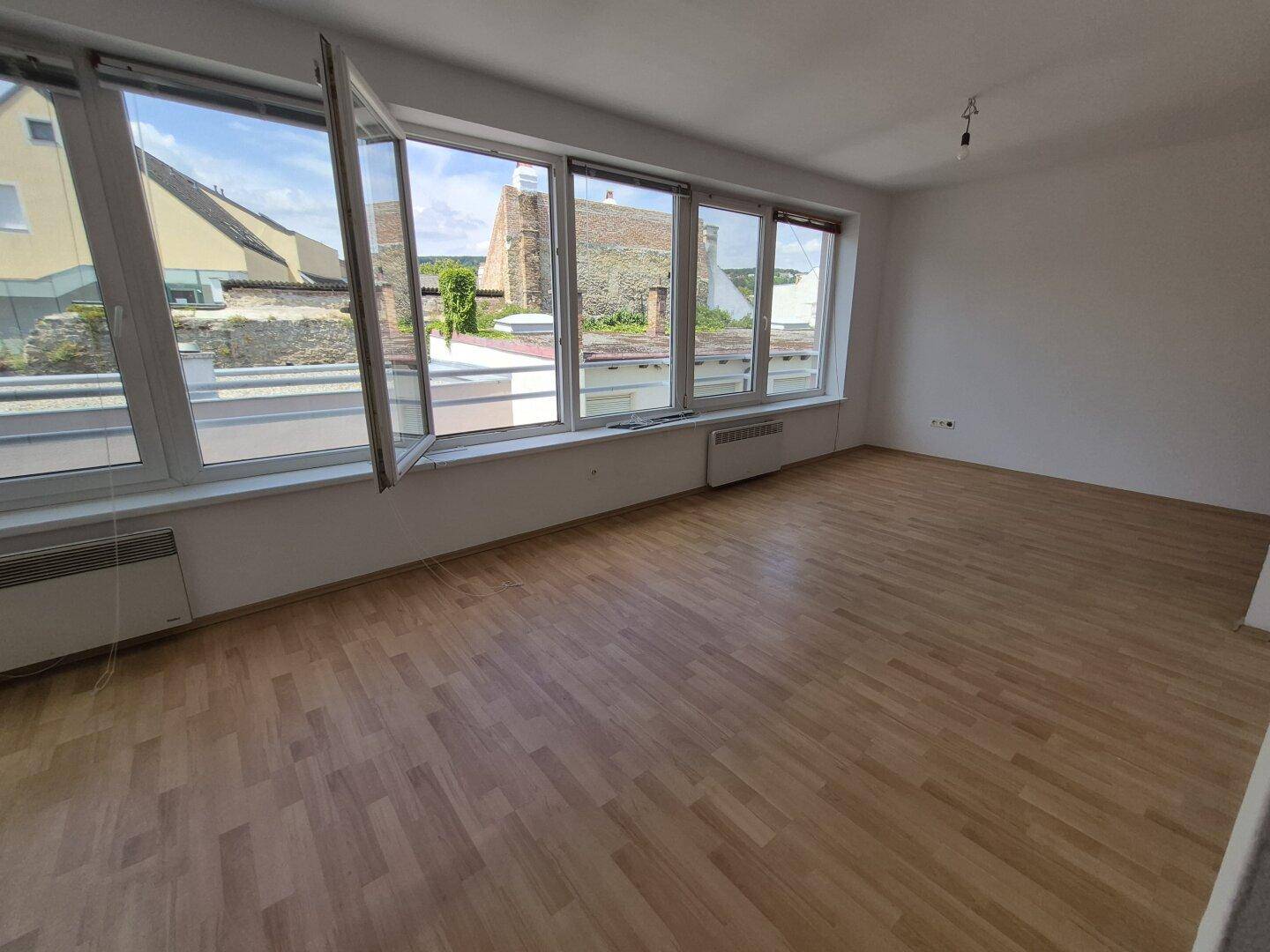Lichtdurchfluteter Raum mit großen Fenstern und Holzparkett, bietet viel Tageslicht und Ausblick.