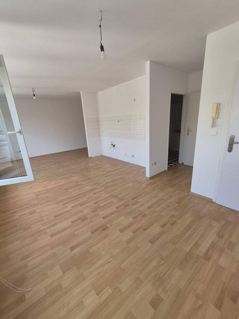 Geräumiger Wohnbereich mit Holzparkett und Anschluss für eine Küche, bietet flexible Gestaltungsmöglichkeiten.