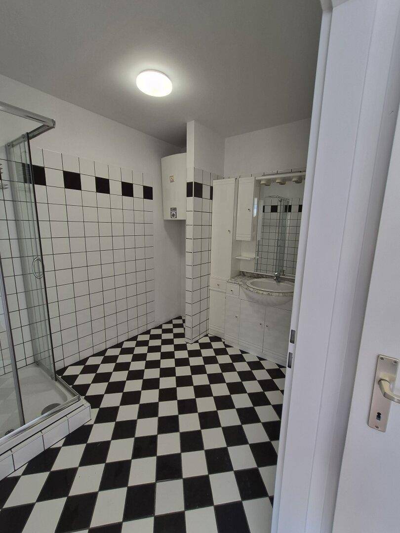 Badezimmer mit schwarz-weißem Fliesenmuster, Duschkabine und Waschtisch mit Spiegelschrank.