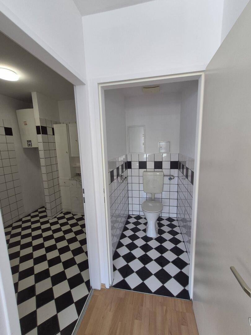 Separates WC mit auffälligem schwarz-weißem Fliesenboden und Wandfliesen.