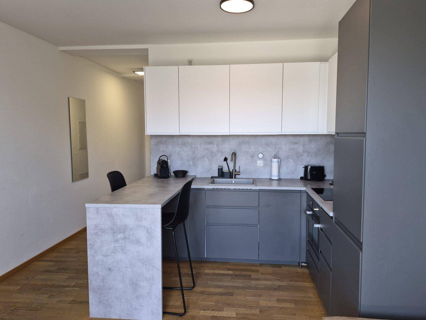 Moderne Küche mit grauen und weißen Schränken, integriertem Tresen und Holzboden.