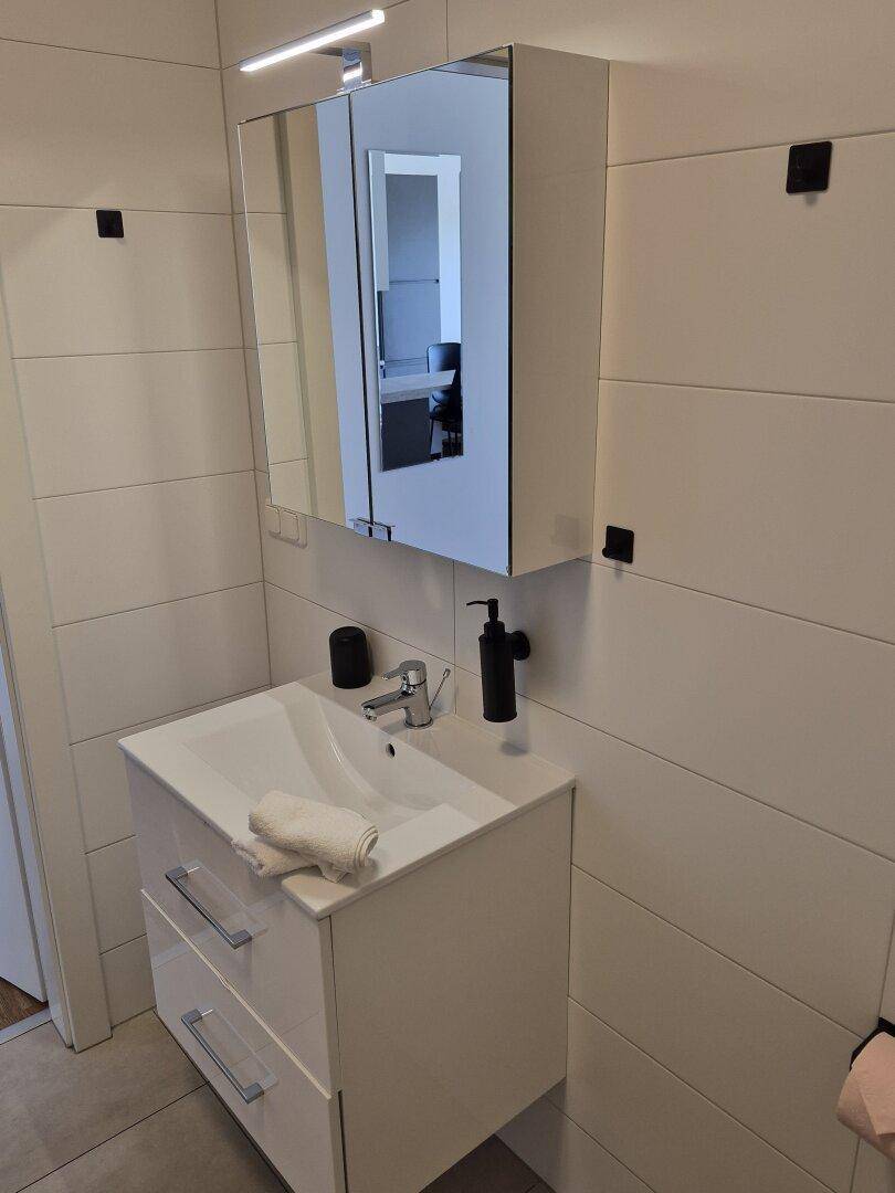 Modernes Badezimmer mit weißen Fliesen, Einzelwaschbecken und Spiegelschrank.