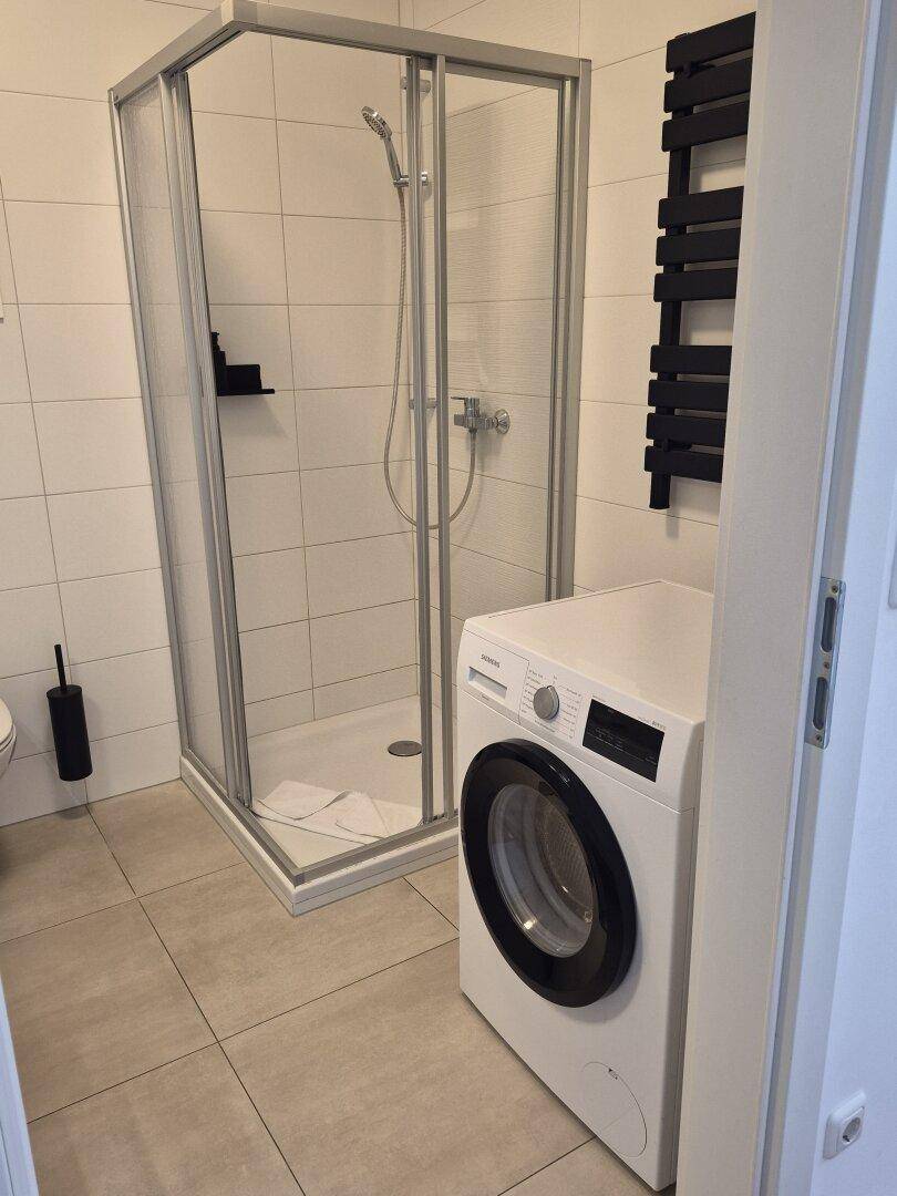 Modernes Badezimmer mit Duschkabine, Waschmaschine und beheiztem Handtuchhalter.