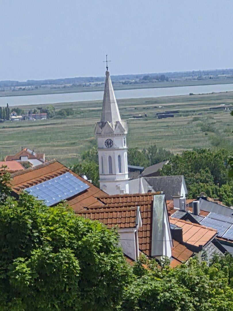 Malerischer Blick auf eine Kirche mit See im Hintergrund und grüner Landschaft.