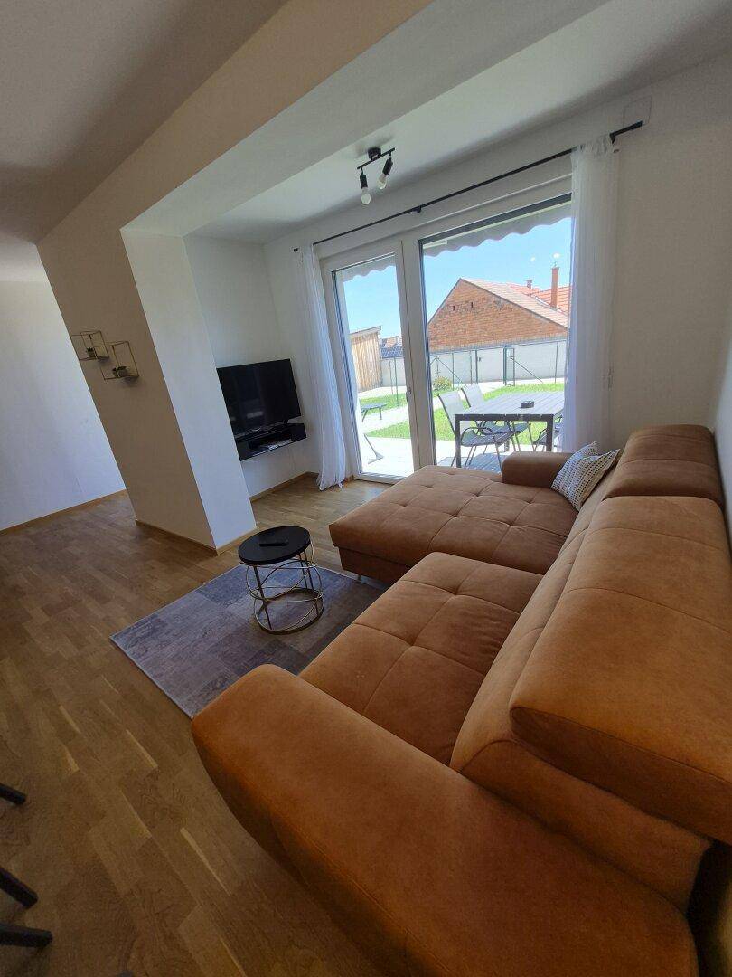 Gemütliches Wohnzimmer mit Sofa, Fernseher und Zugang zur Terrasse oder zum Garten.