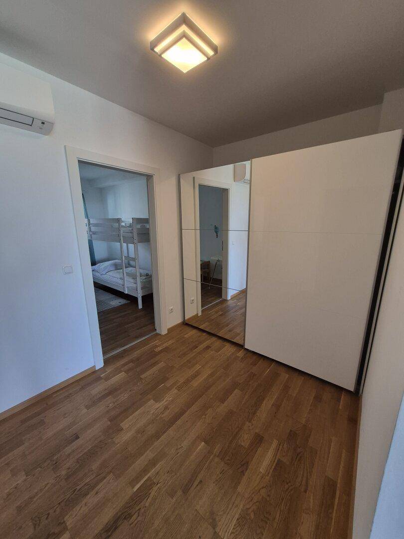 Flur mit Holzboden und Spiegelschrank, der zu den Schlafzimmern führt.