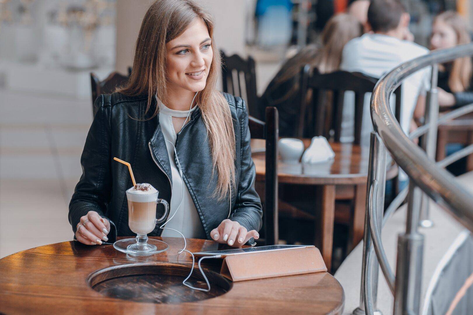 Junge Frau genießt einen Kaffee in einem Café mit Holztischen und gemütlicher Atmosphäre.