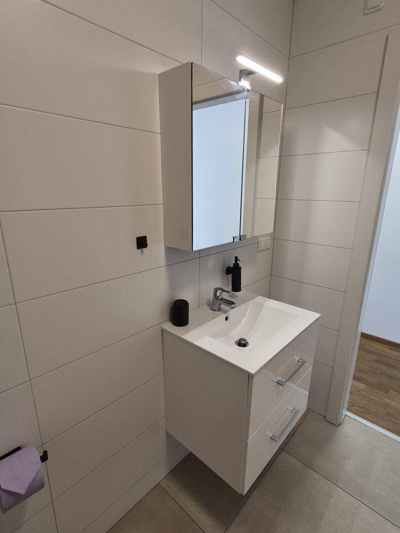 Heller Waschtisch mit Spiegelschrank und modernen Armaturen in einem gefliesten Badezimmer.