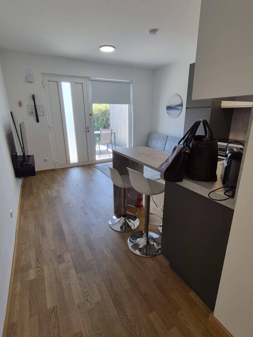 Heller offener Wohnbereich mit Holzboden, Küchenzeile und Zugang zur Terrasse.
