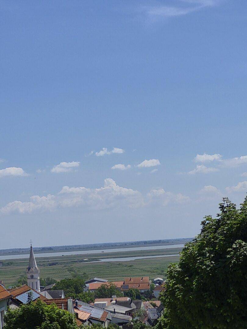 Weitläufiger Blick über eine Stadt, einen See und die umliegende Landschaft unter blauem Himmel.