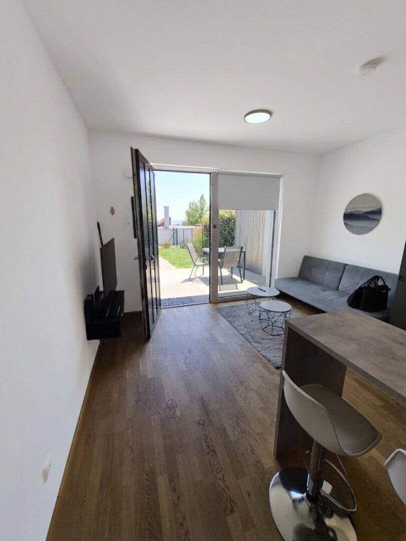 Lichtdurchfluteter Wohnbereich mit Sofa, Fernseher und großem Fenster mit Blick auf den Garten.