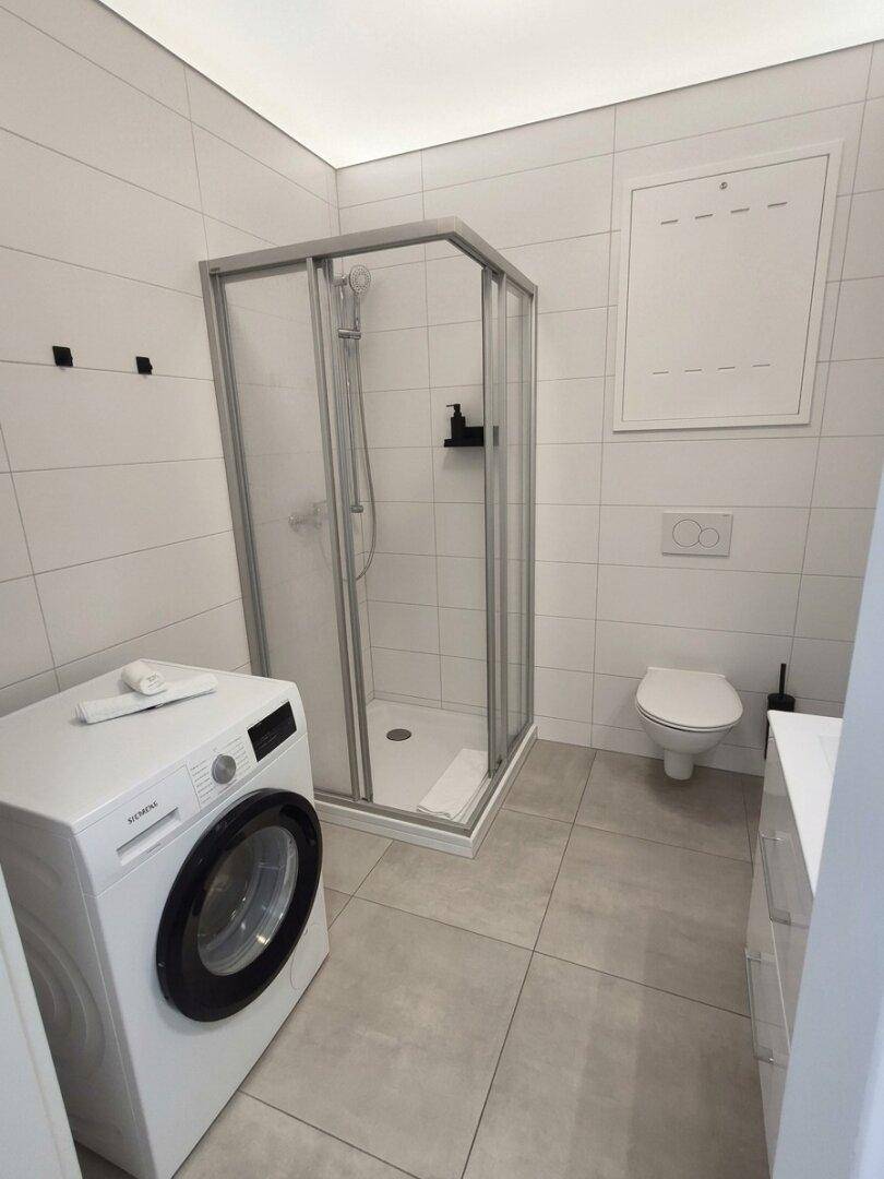 Modernes Badezimmer mit Duschkabine, Toilette und Waschmaschine.