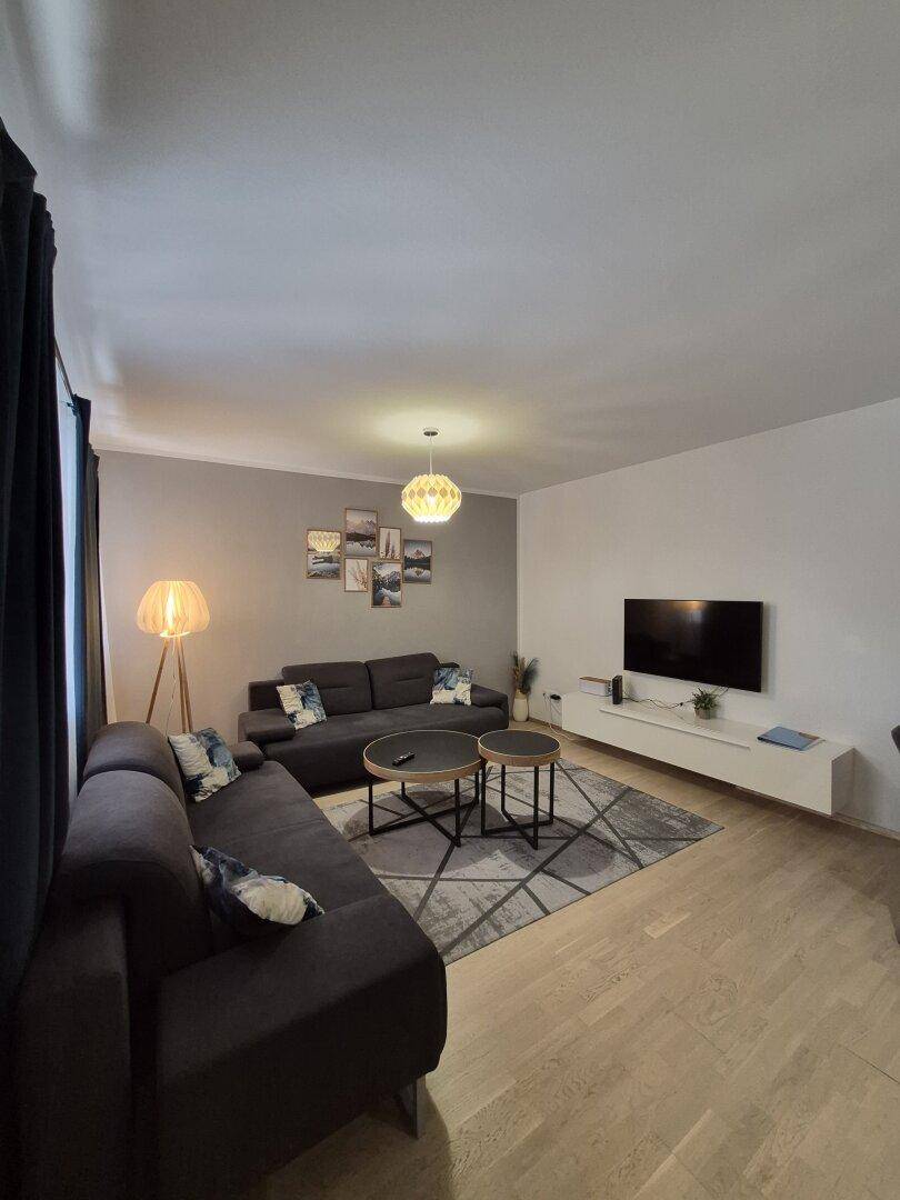 Heller Wohnbereich mit zwei Sofas, Couchtischen und einem Esstisch im Hintergrund, modern eingerichtet.
