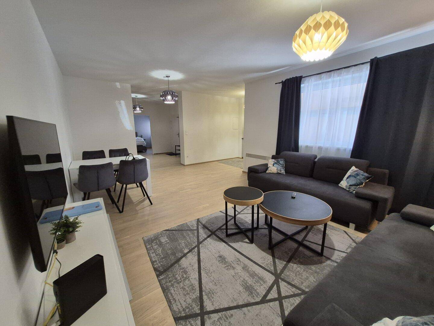 Geräumiger Wohn- und Essbereich mit dunklen Möbeln, Teppich und hellem Laminatboden, gut beleuchtet.