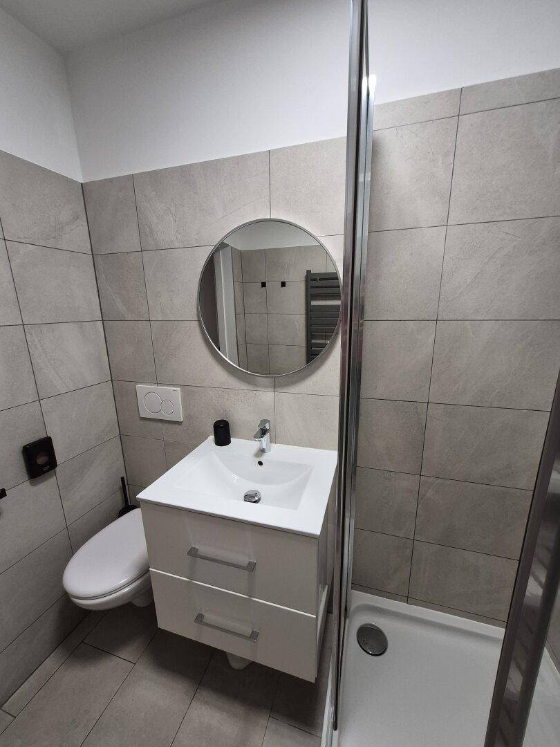 Helles Badezimmer mit wandhängendem WC, modernem Waschbecken und rundem Spiegel.