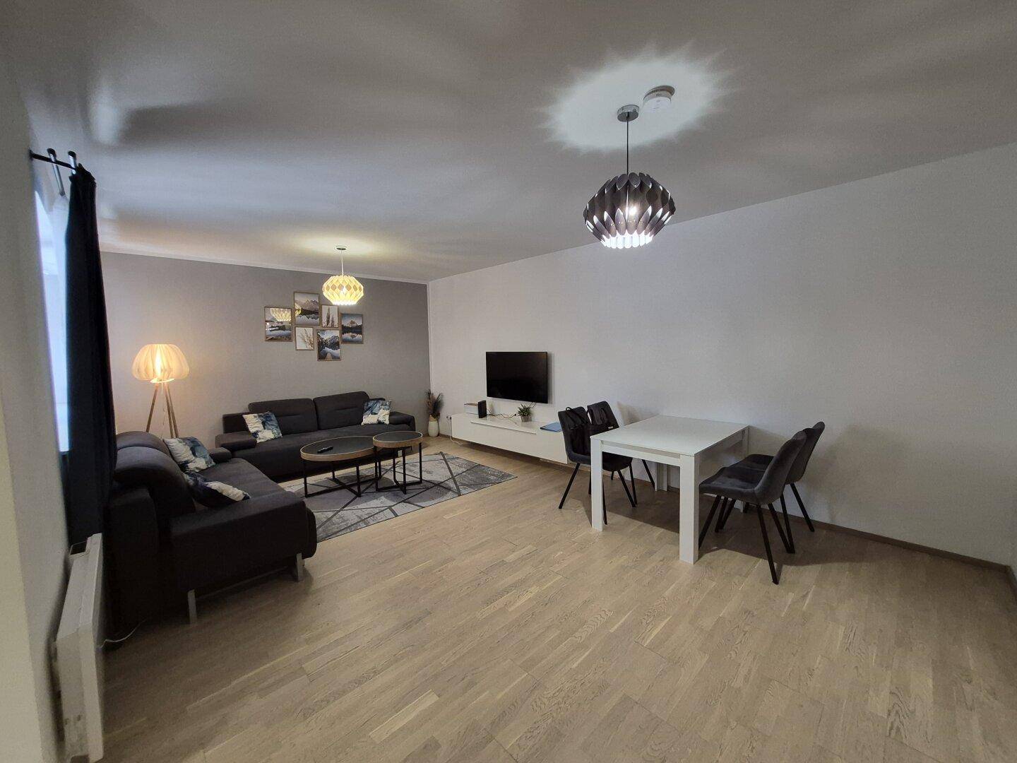 Geräumiger Wohn- und Essbereich mit dunklem Sofa, Esstisch und moderner Dekoration.