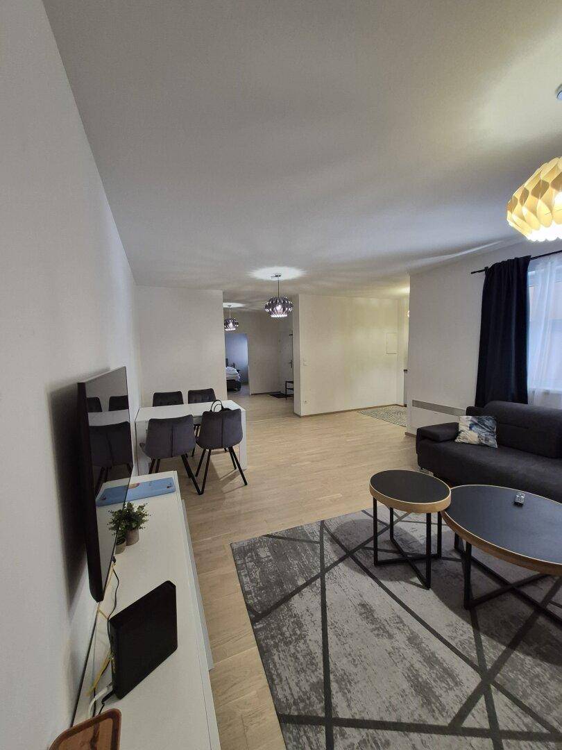 Heller Wohn- und Essbereich mit modernem Sofa, Couchtischen und hellem Holzboden.