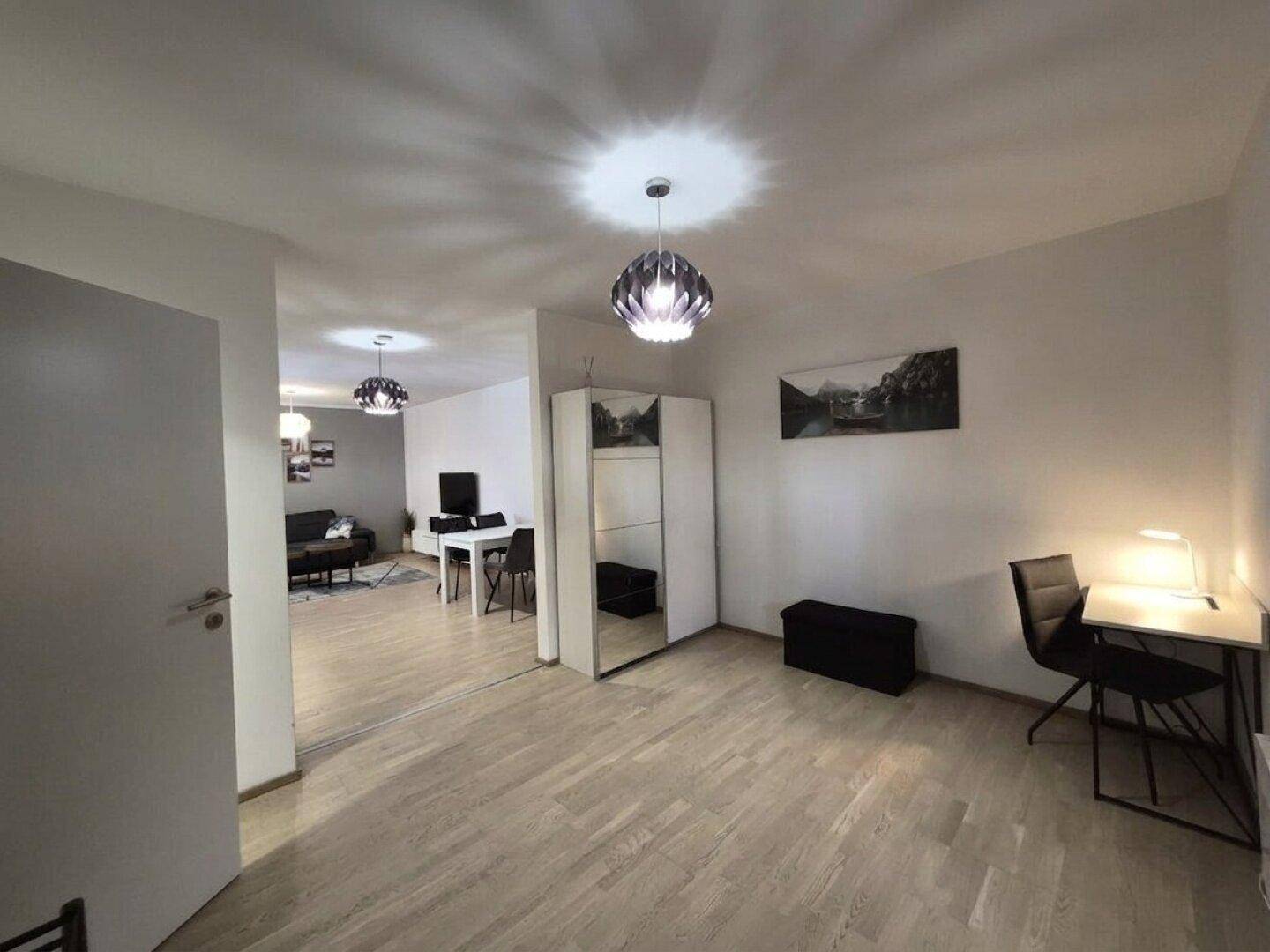 Helles Schlafzimmer mit Holzboden, Schreibtisch und Kleiderschrank, offen zum Wohnbereich.