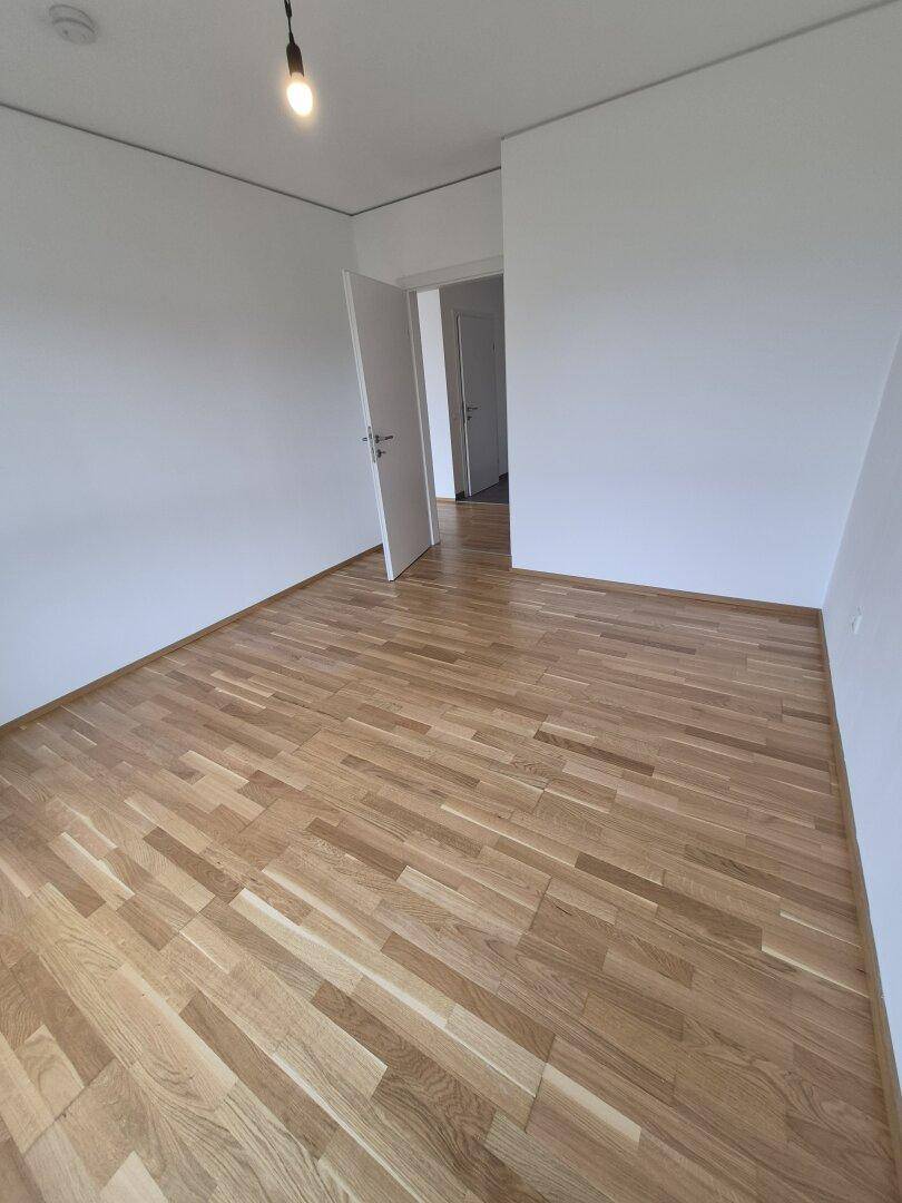 Leeres Zimmer mit Parkettboden und weiß gestrichenen Wänden, bereit zur Einrichtung.