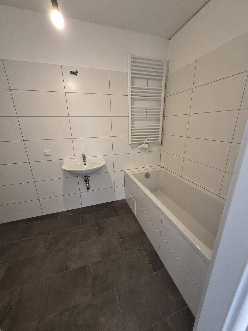 Modernes Badezimmer mit Badewanne, Waschbecken und weiß-grauen Fliesen.