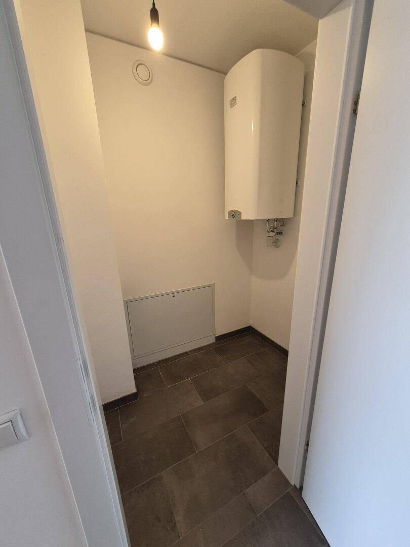 Kleiner Abstellraum mit Warmwasserboiler und dunklen Bodenfliesen.