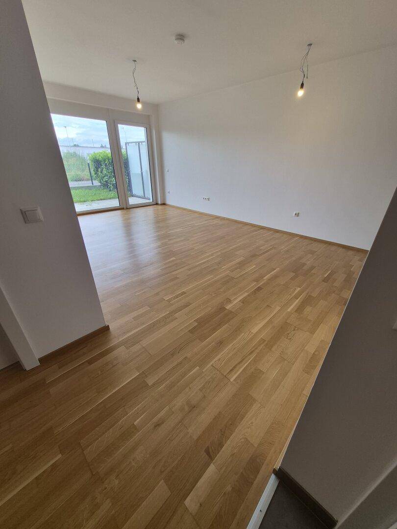 Heller, leerer Wohnraum mit Eichenparkettboden und großen Fenstern zum Garten.