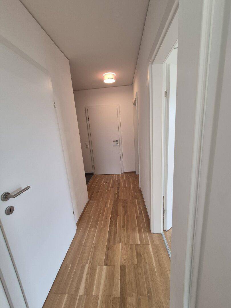 Langer, heller Flur mit Holzparkettboden und mehreren weißen Türen.