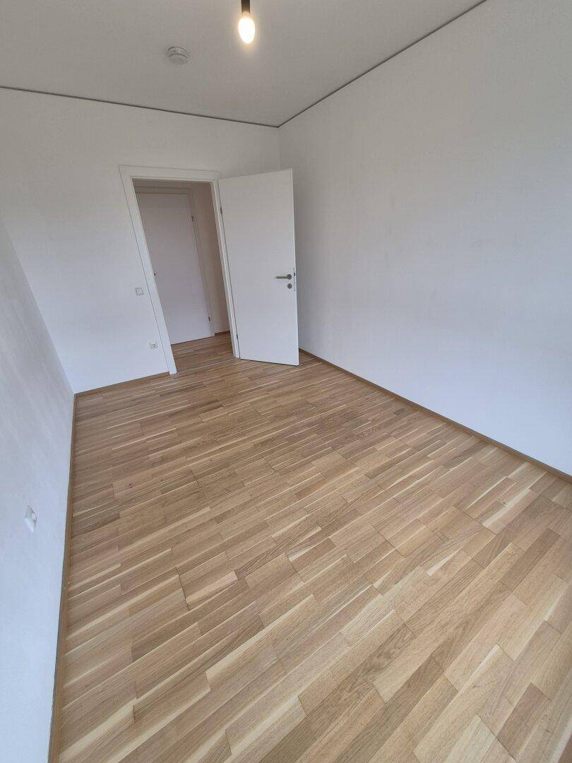 Leeres Schlafzimmer mit hellem Holzparkettboden und weiß gestrichenen Wänden.