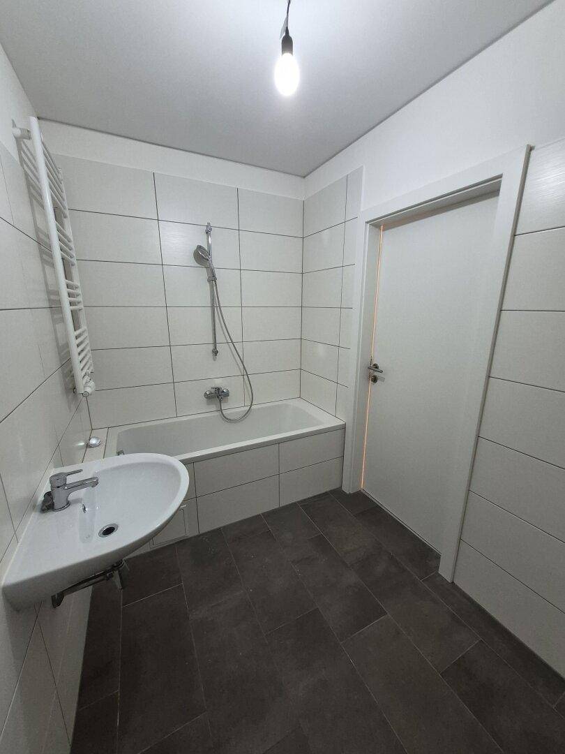 Modernes Badezimmer mit Badewanne, Waschbecken, weißen Fliesen und beheiztem Handtuchhalter.