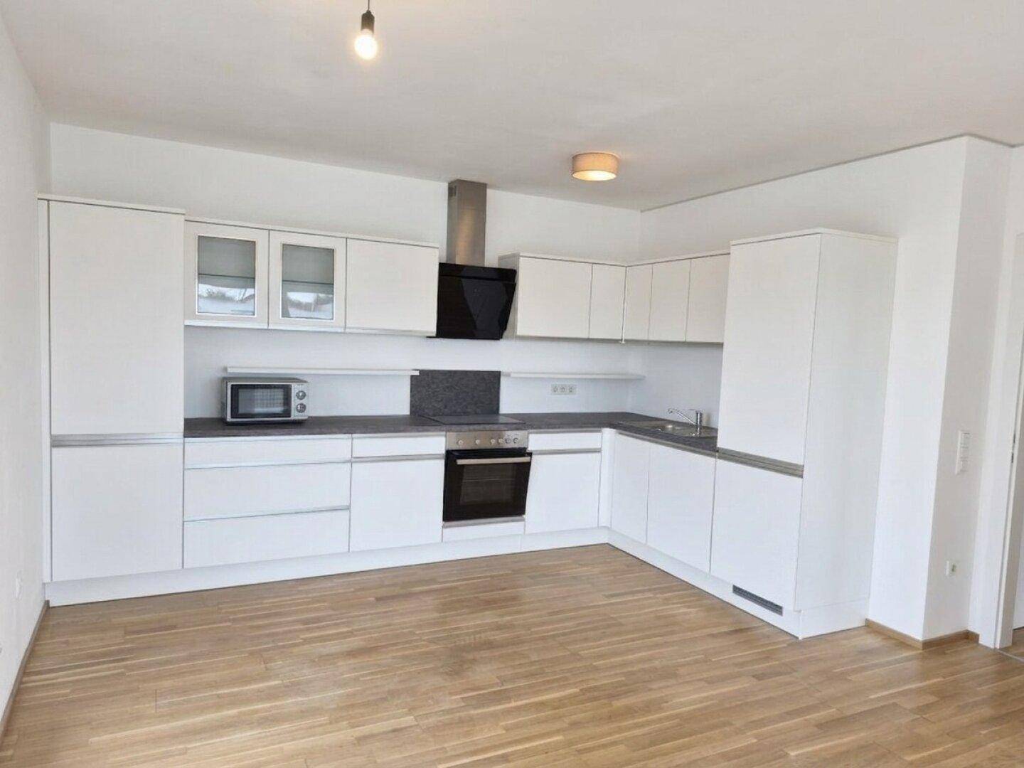 Moderne Einbauküche in Weiß mit integrierten Geräten und hellem Holzparkettboden.