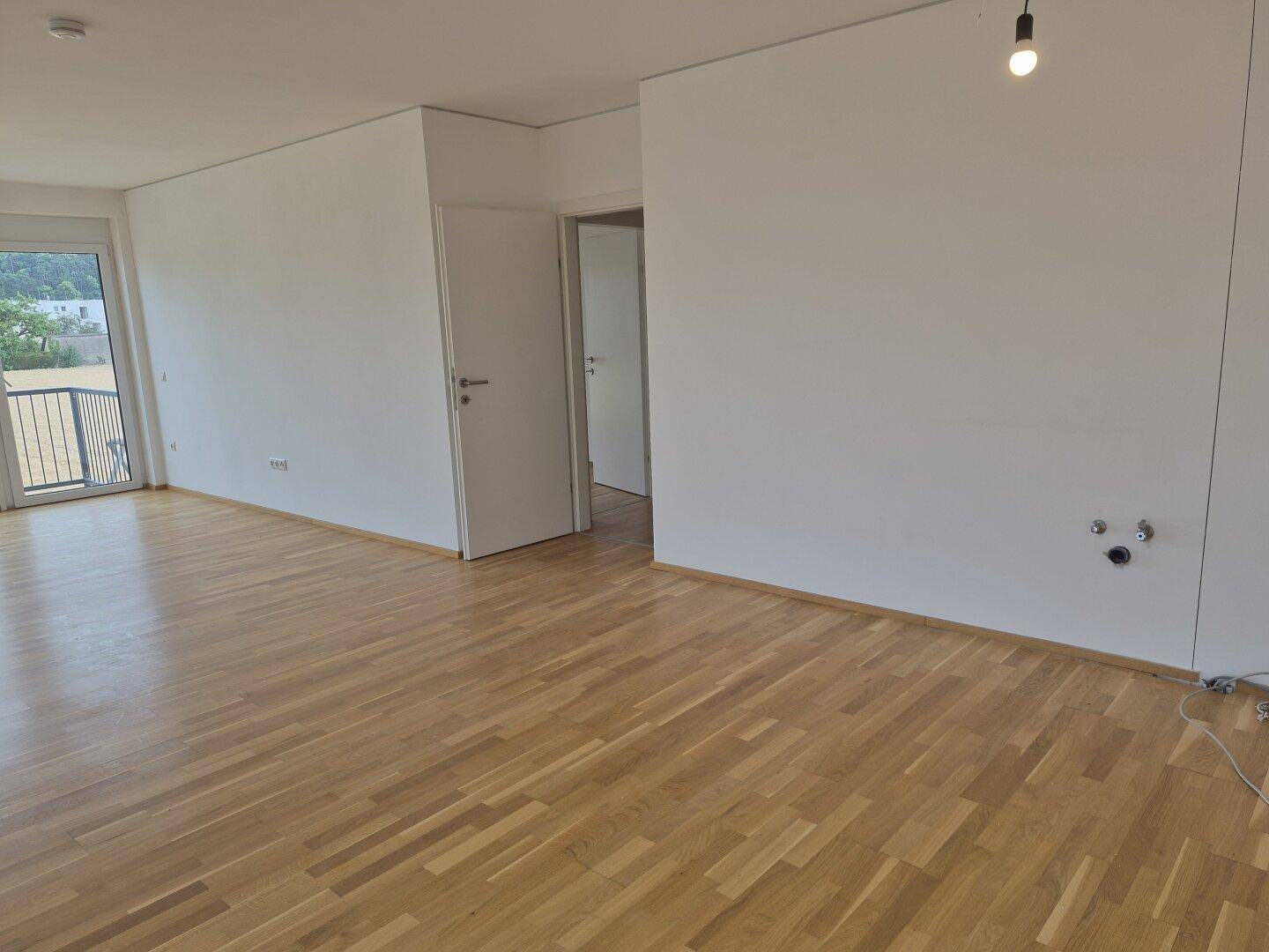Geräumiger Wohnbereich mit Parkettboden und Zugang zu einem Balkon.