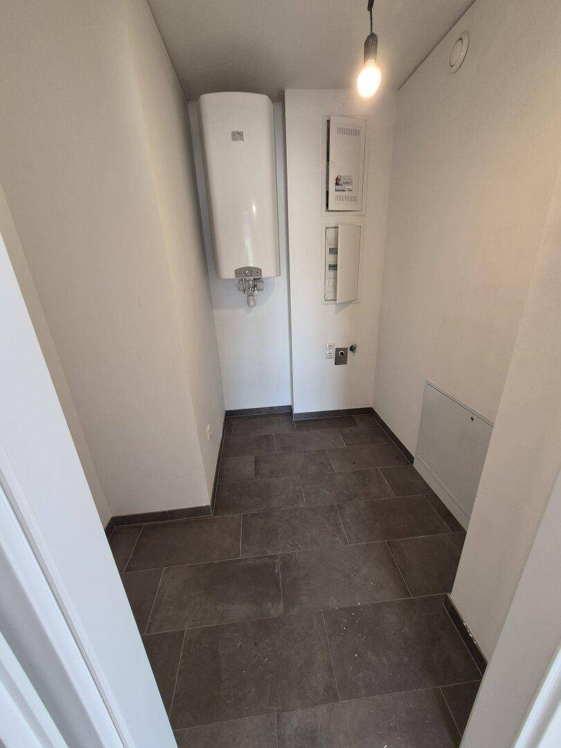 Praktischer Hauswirtschaftsraum mit Fliesenboden, Warmwasserbereiter und Elektroinstallationen.