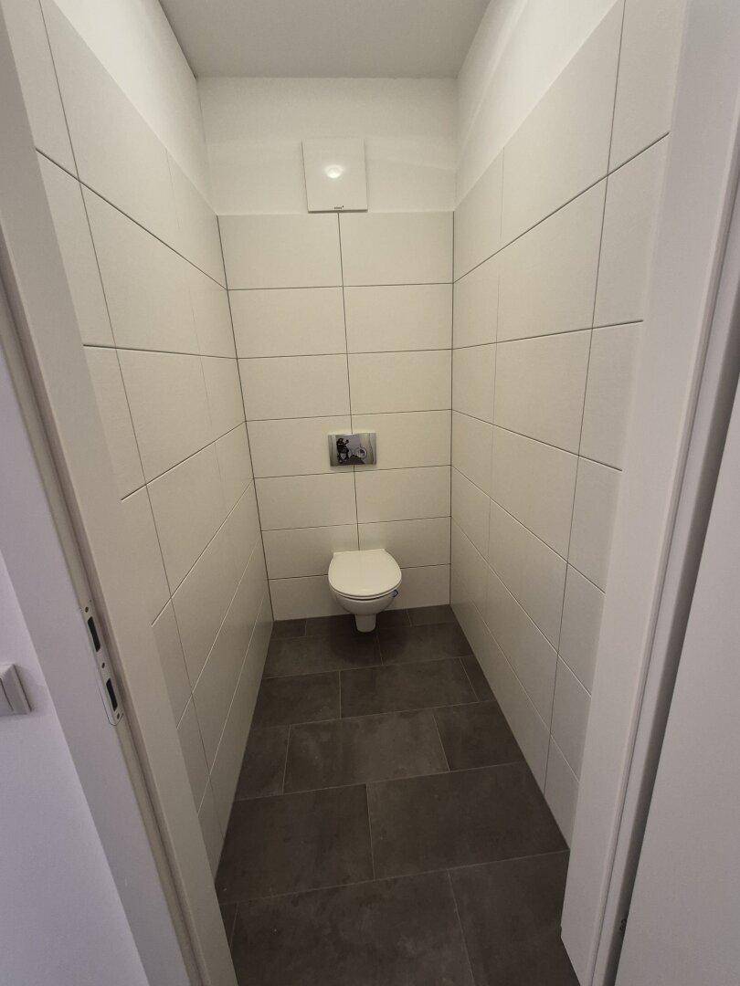 Modernes Gäste-WC mit wandhängender Toilette und weißen sowie dunklen Fliesen.